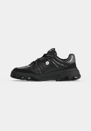 Sneaker nero low-top con suola spessa, allacciatura frontale e dettaglio metallico sul tallone, vista laterale su sfondo bianco.