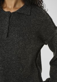 Close-up of a person wearing a dark gray knit sweater with a collar and three black buttons on the front.