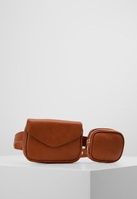 Ruskea nahkainen vyölaukku, jossa on kaksi taskua: yksi suorakaiteen muotoinen läpällä ja toinen pienempi pyöreä vetoketjulla, esillä valkoisella pinnalla.