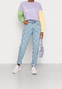 Sudadera en bloques de color lavanda, verde y amarillo; vaqueros a cuadros azul claro de talle alto; zapatillas pastel; bolso pequeño morado.