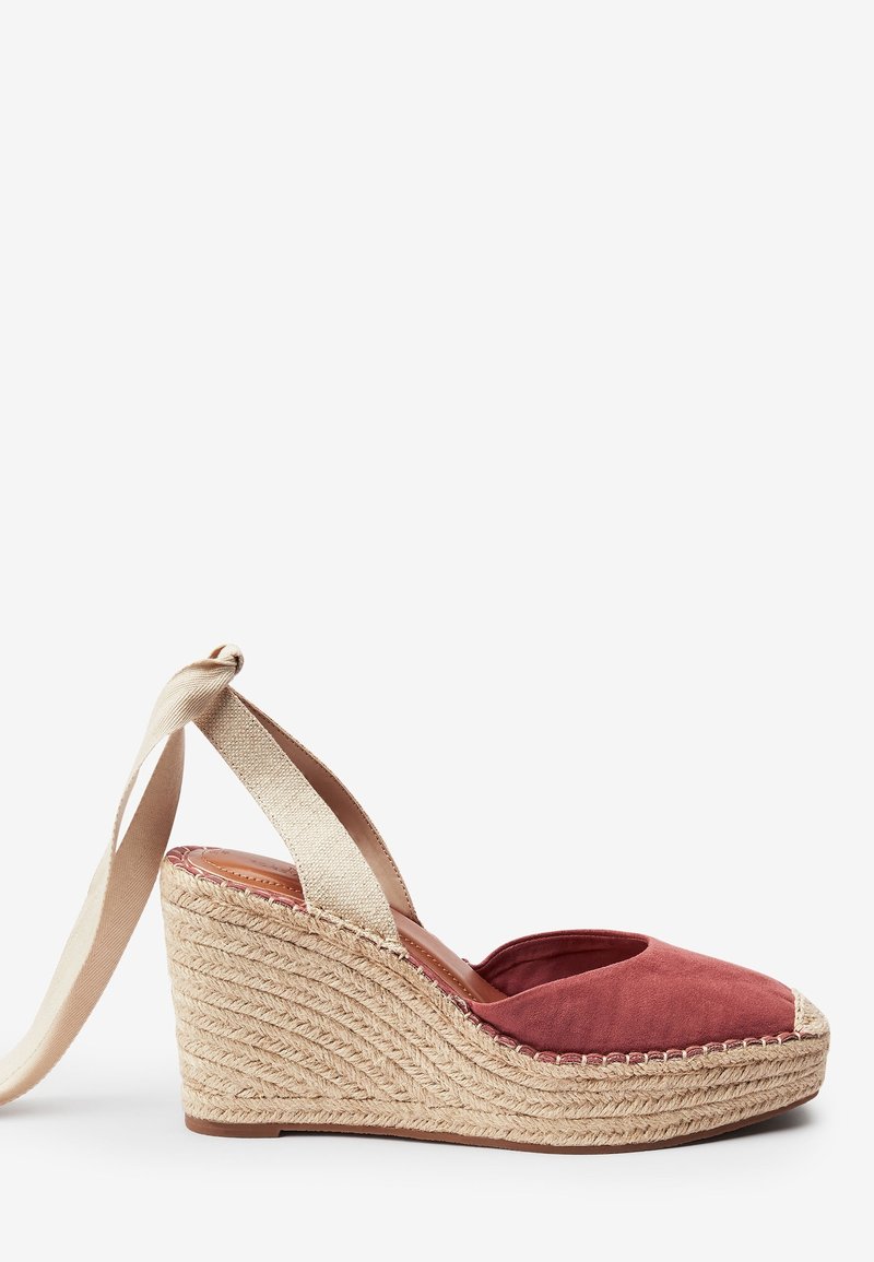 Espadrille compensée avec un dessus en daim bordeaux et des lanières de cheville en tissu beige. Présente une semelle intermédiaire en jute naturel et un design à bout rond.