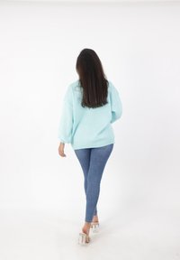 Maglione oversize azzurro chiaro a maglia con finitura texturizzata, abbinato a jeans skinny e sandali con tacco trasparente.