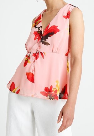Blouse fleurie rose avec un décolleté en V, des manches courtes et une coupe ample évasée. Motifs de fleurs rouges et jaunes. Tissu léger.