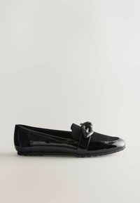 Sorte flade sko med en blank lakeret finish, suede detaljer og en dekorativ knude på forsiden. Har en afrundet tå og en fleksibel sål.