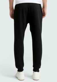 Joggers negros de tela suave, con piernas ajustadas, puños elásticos y cintura con cordón, combinados con zapatillas blancas.