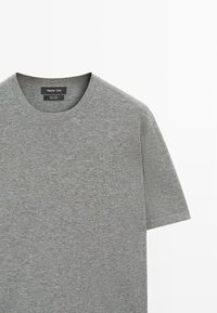 Schlichtes graues Kurzarm-T-Shirt aus Baumwolle mit rundem Halsausschnitt und sichtbarem Markenetikett, das im Nackenbereich eingenäht ist.