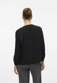 Maglione nero a maniche lunghe con punti testurizzati, scollatura rotonda e vestibilità comoda. Indossato con pantaloni grigi, che mostrano un design minimalista.
