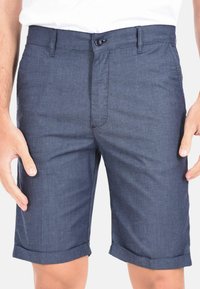 Pantaloni corti blu navy realizzati in un tessuto tessuto con texture, dotati di chiusura con bottone e risvolti, che evidenziano un design su misura.