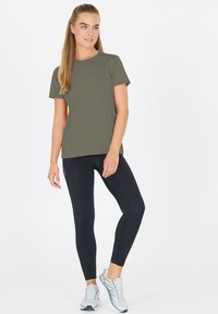 Olivgrön t-shirt med kort ärm i sportstil, kombinerad med svarta leggings och ljusgrå löparskor, med en figurnära design och slät textur.