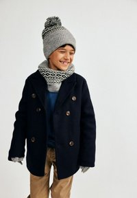 Tumesinine villane mantel topelt-nupudega, hall kudumüts pom-pomiga, mustriga sall, kindad ja beežid püksid.