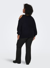 Pull noir en maille avec design à épaules dénudées, associé à un pantalon noir évasé. Le pull présente une coupe ample et un tissu texturé.