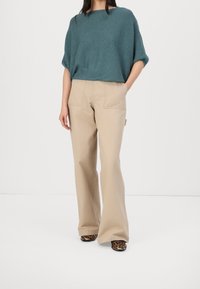 Türkis strukturierter Pullover, beige weit geschnittene Hose mit zwei vorderen Taschen und schwarze Schuhe mit Leopardenmuster. Einfaches, lässiges Outfit-Design.