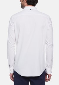 Witte longsleeve shirt met een gladde textuur, een standaardkraag en met knopen gesloten manchetten. Heeft een subtiele logodetail aan de achterkant en een gebogen zoom.