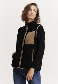 Gilet in pile nero con colletto alto, dotato di tasca sul petto in nylon beige e rifiniture a contrasto beige. Design casual con tasche laterali.