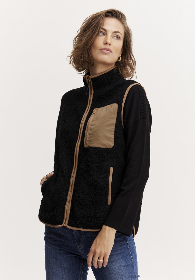 Svart fleeceväst med hög krage, försedd med ett brunt nylon bröstficka och kontrasterande brunt kantband. Avslappnad design med sidofickor.