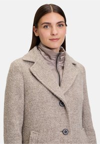 Beige wollen blend jas met een gestructureerde afwerking, revers kraag en twee zwarte knopen. De binnenkant heeft een lichtgewicht, met rits gesloten, grijze gewatteerde laag.