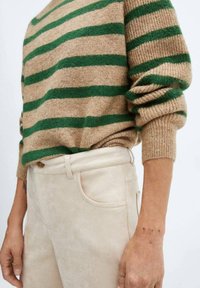 Maglione a maglia con strisce orizzontali verdi e beige, abbinato a pantaloni color crema con bottone e tasche frontali.