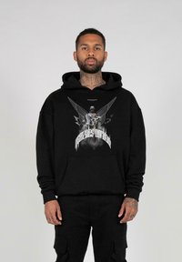 Schwarzer Hoodie mit einem Frontdruck, der Flügel und eine Figur zeigt. Das Material wirkt weich. Einfaches Design mit Kapuze und Kängurutasche.