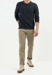 Pull ras du cou marine, chinos beige et baskets crème. Le pull présente des poignets et un ourlet côtelés. Les chaussures ont une semelle texturée.