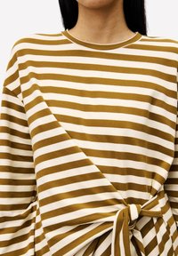 Gestreepte langemouwen top met afwisselend mosterd- en witte strepen, een ronde halslijn en een strikdetail in de taille. Zachte stoftextuur.