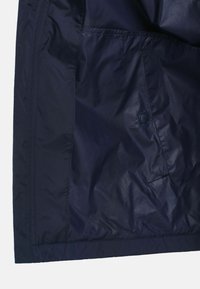 Námorně modrá lehká tkanina s hladkým povrchem, obsahující boční kapsu a patentní knoflík. Viditelné švy a čisté okraje.
