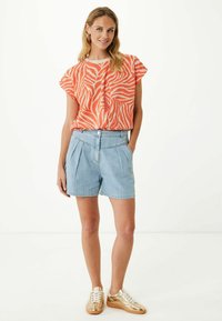 Hnědo-oranžový top s krátkým rukávem ve zebřím vzoru, zkombinovaný se světle modrými skládacími šortkami. Doplňuje jej zlaté tenisky s bílými tkaničkami.