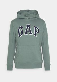 Felpa verde con cappuccio e tasca a marsupio, con un grande logo "GAP" blu navy sul davanti. Tessuto morbido e polsini a coste sulle maniche e sull'orlo.