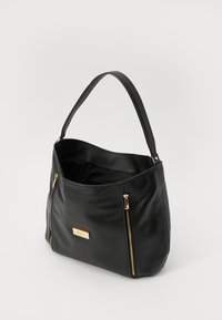 Sac en cuir noir au toucher lisse, de forme courbée, avec des accents dorés et deux poches zippées à l'avant. Intérieur spacieux.