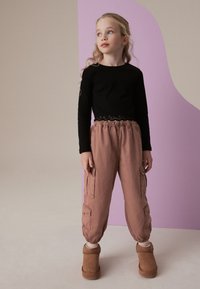 Juodas ilgos rankovės viršus su nėrinių apdaila, derinamas su rožiniais cargo tipo džinsais, kurie turi šonines kišenes ir elastingus rankogalius. Rudi auliniai batai užbaigia aprangą.