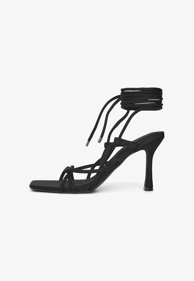 Sandale noire à talons hauts avec des fines brides entrecroisées et un design épuré. Présente une pointe carrée et plusieurs liens à la cheville. Texture lisse.