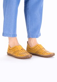 Gelbe Leder-Pantoletten mit Cut-out-Designs, runden Zehen und braunen Gummisohlen. Mit einer dekorativen Naht entlang der Sohle.