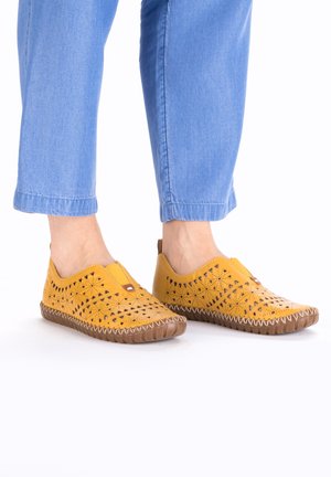 Chaussures à enfiler en cuir jaune avec des découpes, bout rond et semelles en caoutchouc marron. Elles présentent un détail de couture le long de la semelle.