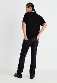 Camisa preta de mangas curtas com textura em canalé, combinada com jeans de perna reta azul-escuro com costuras laranja e desenhos de bolsos traseiros curvados. Sapatos pretos.