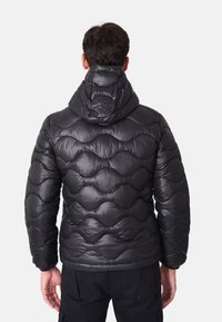 Giacca a vento nera con motivo a onde trapuntato, dotata di cappuccio e texture lucida e liscia. La vista posteriore mostra un design aderente e un orlo dritto.