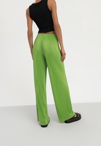 Pantaloni larghi a coste di un verde chiaro con vita alta, abbinati a un top senza maniche nero e sandali con piattaforma, visti da dietro.
