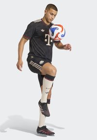 Male soccer player in black kit controlling a red, white, and blue ball with his raised knee.