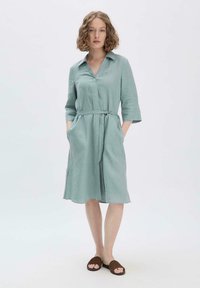 Helles Türkis-chemise mit Kragen, Dreiviertel-Ärmeln, gebundenem Taillenbund und seitlichen Taschen. Weicher, strukturierter Stoff, der knapp über dem Knie fällt.