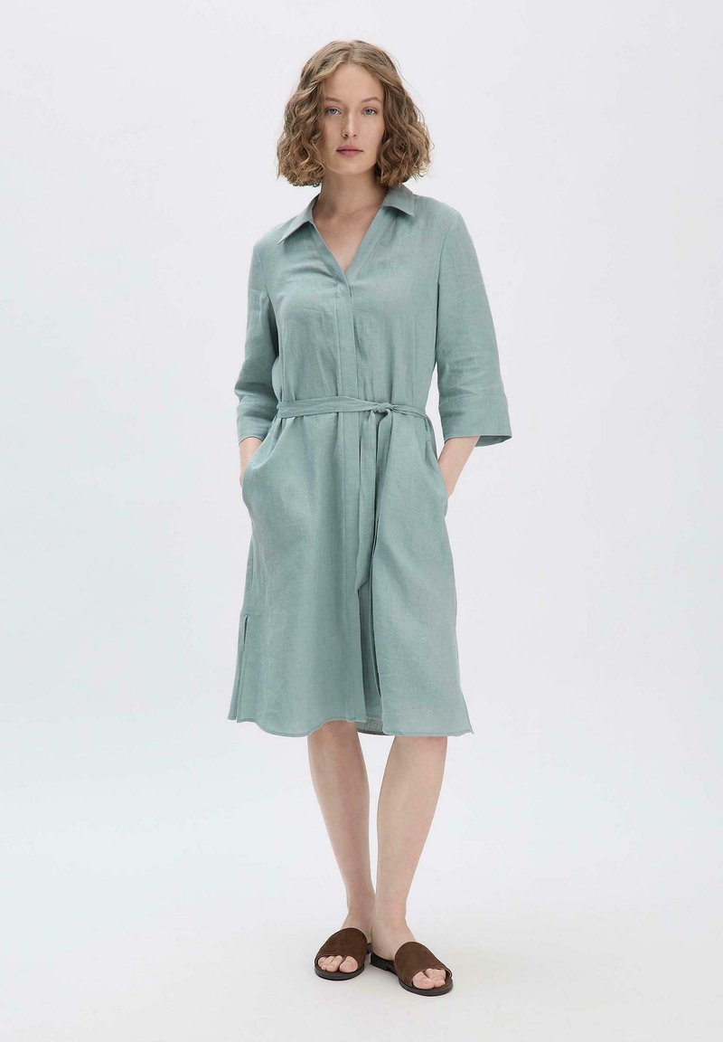Helles Türkis-chemise mit Kragen, Dreiviertel-Ärmeln, gebundenem Taillenbund und seitlichen Taschen. Weicher, strukturierter Stoff, der knapp über dem Knie fällt.