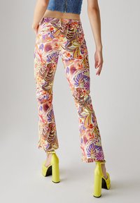 Pantaloni a zampa d'elefante in stampa floreale multicolore, con vita alta, motivi vivaci e materiale leggero. Indossati con scarpe a blocco gialle.