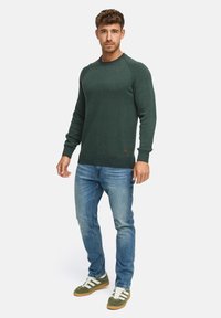 Mørkegrøn striktrøje med rund hals, ribbet manchet og kant. Kombineret med lyseblå jeans og grønne sneakers med hvide striber.