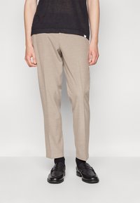 Licht beige op maat gemaakte broek met een rechte snit, gemaakt van gladde stof. Gecombineerd met zwarte instappers en donkere sokken, met een minimalistisch ontwerp.