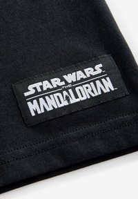 Mustat puuvillapaidat, joissa on "STAR WARS THE MANDALORIAN" valkoisella tekstillä kudotussa tarrassa, jossa on ommeltu reuna.