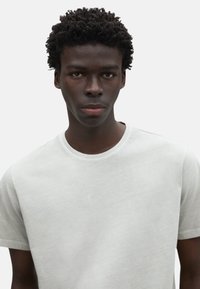 Camiseta de cuello redondo en gris claro, hecha de una tela suave, con mangas cortas y una textura lisa sin patrones ni detalles adicionales.