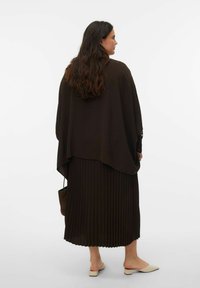 Tenue marron à couches comprenant un haut long et fluide et une jupe plissée. Texture de tissu lisse avec un motif subtil en forme de vague. Chaussures de couleur claire.