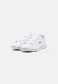 Vita sneakers gjorda av slätt syntetmaterial, med snörningsdesign, rund tå och en liten grön logotyp på sidan.