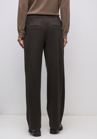 Breda byxor i mörkbrun färg med elastisk midja och två bakfickor. Slät textur och skräddarsydd passform. Perfekta för avslappnad klädsel.