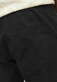 Pantalones cortos de algodón negros con un bolsillo trasero visible. La tela tiene una textura suave y un diseño simple y limpio.