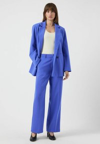 Blå skreddersydd dress laget av glatt stoff, med en dobbeltspent blazer med brede slag og vide, rette bukser.