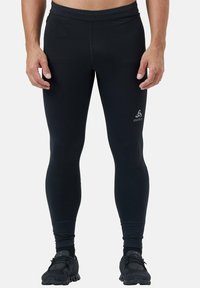 Zwarte legging gemaakt van rekbaar materiaal, met een gladde textuur en een aansluitend ontwerp. Logo gedrukt op de linker dye, geen zichtbare patronen of hardware.