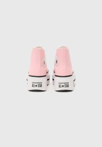 Pink canvas high-top sneakers with white sole, featuring black accents and a circular logo on the heel. Classic Converse design.